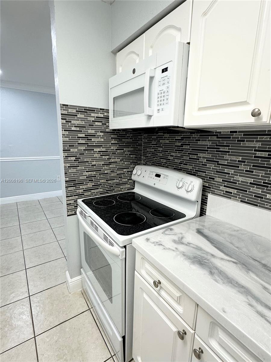 A kitchen features white cabinets, a glass-top stove, a microwave, and a dark mosaic backsplash — 9405 SW 76th St # Y32, Miami FL 33173, MIAMI, FL