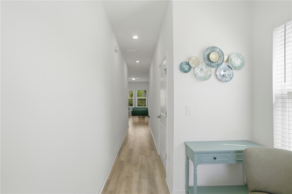 A hallway with light wood flooring leads toward a room with green furniture — 1794 SUNDANCE CHASE ROAD, MINNEOLA, FL