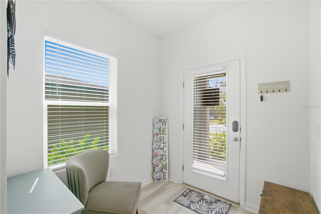 A bright entryway features a gray armchair, a welcome sign, and a glass-paneled front door — 1794 SUNDANCE CHASE ROAD, MINNEOLA, FL