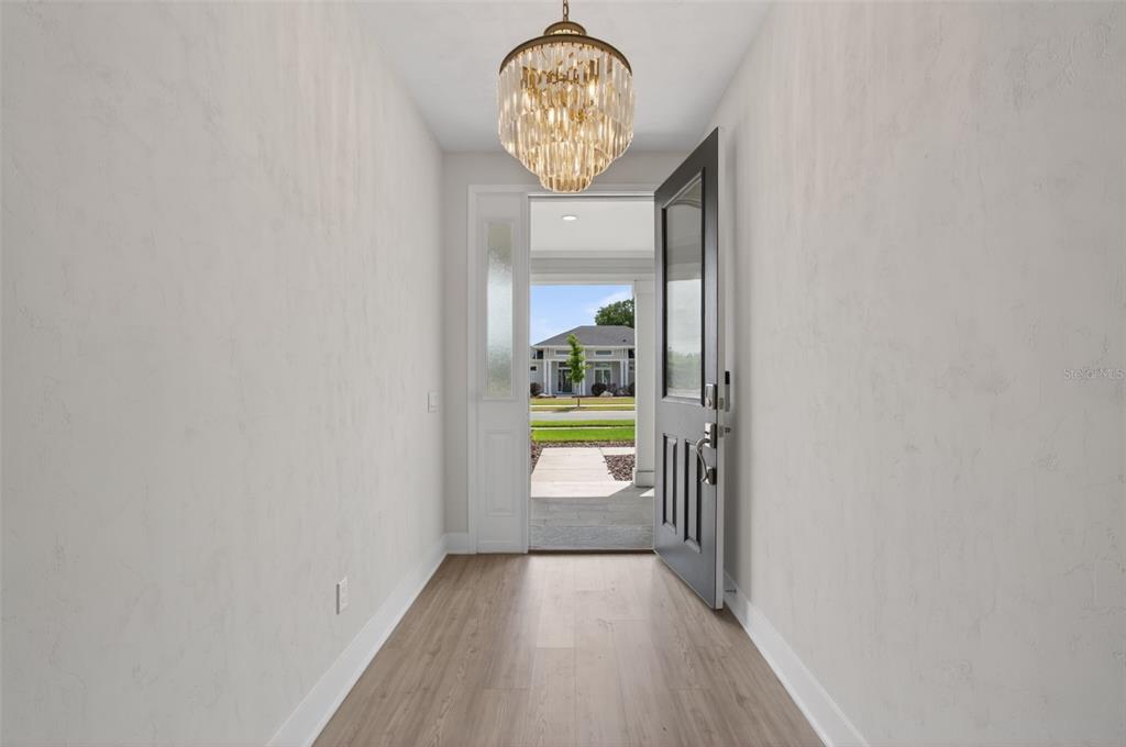 A bright entryway features light wood flooring, a crystal chandelier, and an open front door — 428 SW 144TH DRIVE, NEWBERRY, FL