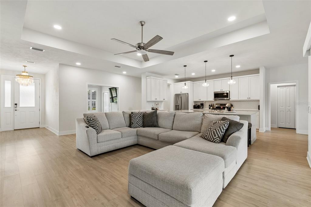A spacious open-concept living room features a large sectional sofa, light wood floors, and kitchen — 428 SW 144TH DRIVE, NEWBERRY, FL