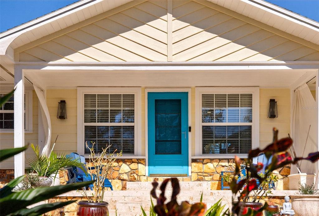 A yellow house exterior features a bright blue front door and a stone porch base — 504 BAYVIEW PARKWAY, NOKOMIS, FL