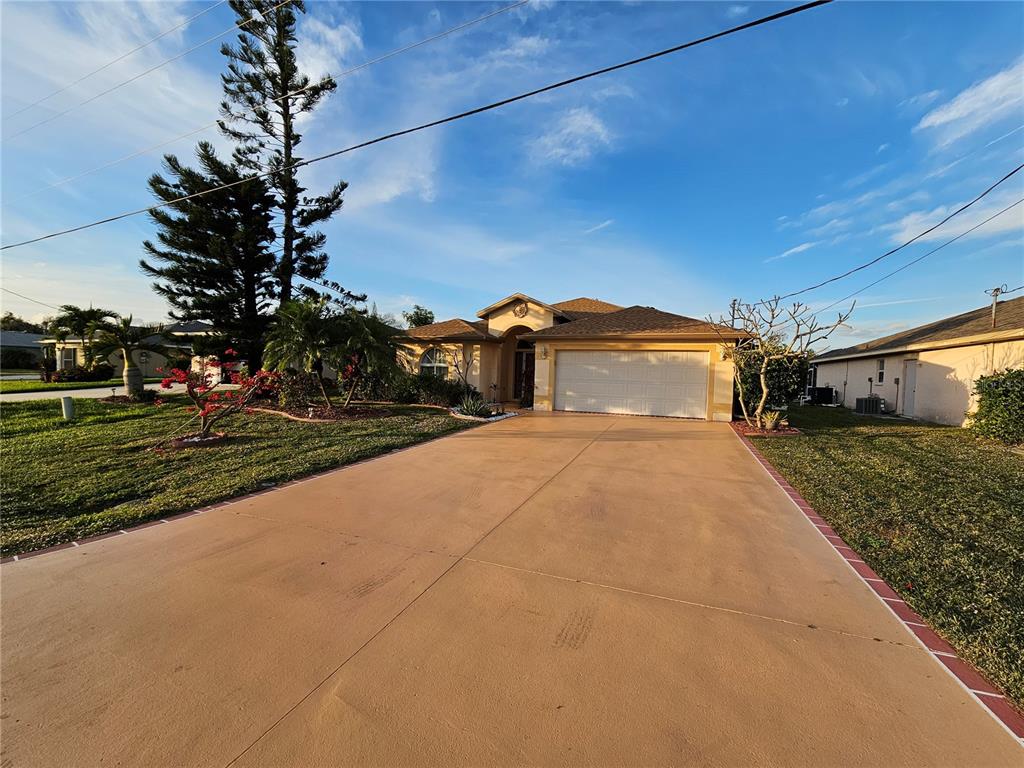 A single-story house with a tan exterior, a two-car garage, and a large concrete driveway — 114 ALBATROSS ROAD, ROTONDA WEST, FL