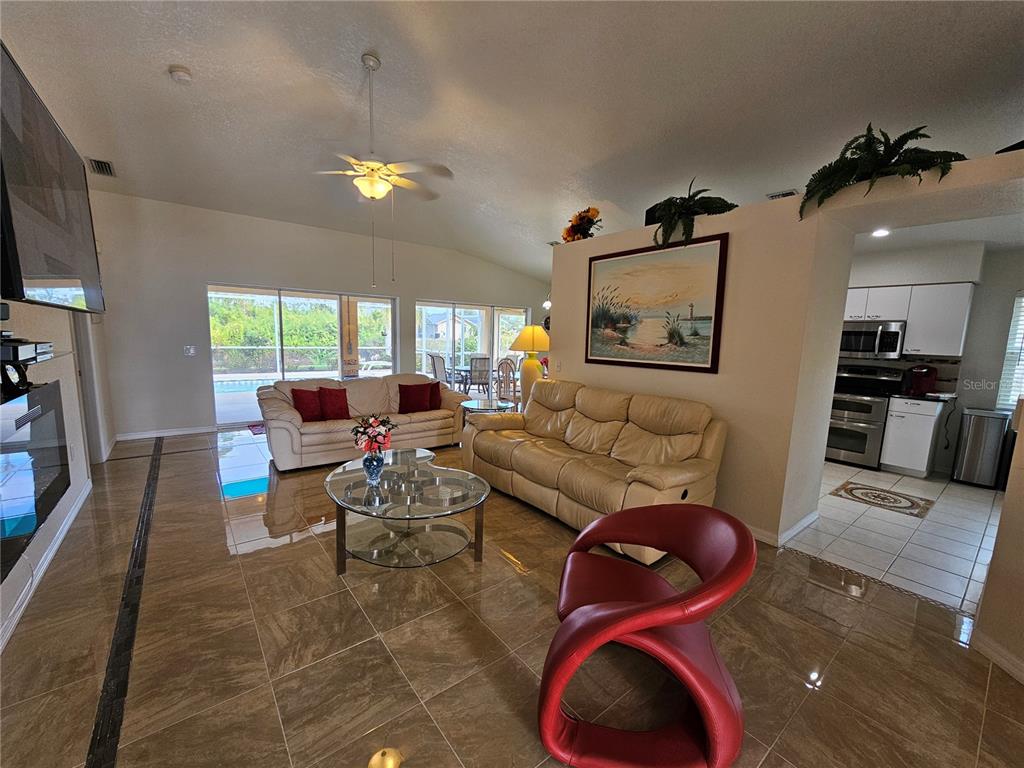 A living room features tile flooring, two sofas, a red accent chair, and a kitchen — 114 ALBATROSS ROAD, ROTONDA WEST, FL
