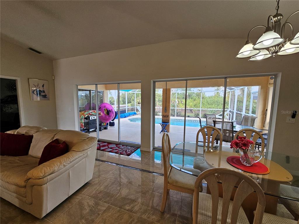 A living and dining area with tile floors, sliding glass doors, and a backyard pool — 114 ALBATROSS ROAD, ROTONDA WEST, FL