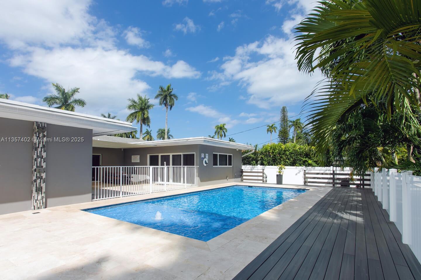 A rectangular swimming pool sits in a backyard with a stone patio and wooden deck — 1218 Hollywood Blvd, Hollywood FL 33019, HOLLYWOOD, FL