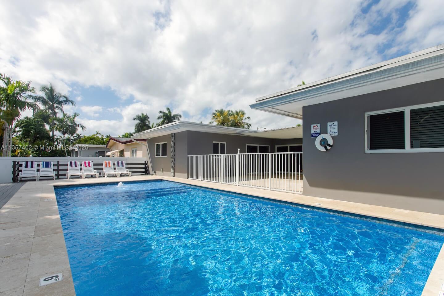 A rectangular swimming pool sits in a backyard patio area next to a gray house — 1218 Hollywood Blvd, Hollywood FL 33019, HOLLYWOOD, FL