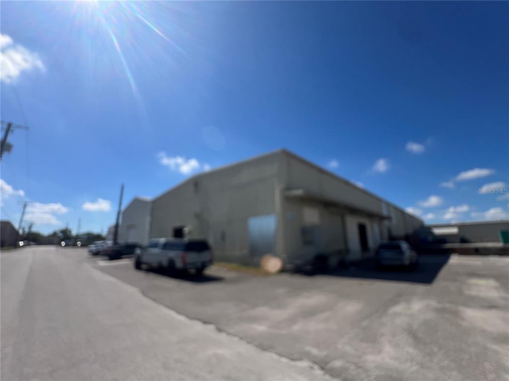 A low-rise industrial warehouse building with a paved parking lot under a blue sky — 5705 E HANNA AVENUE, TAMPA, FL