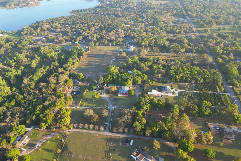 An aerial view shows a rural property with multiple buildings, pastures, and trees near water — 280 CAMPBELL RANCH RUN, GENEVA, FL